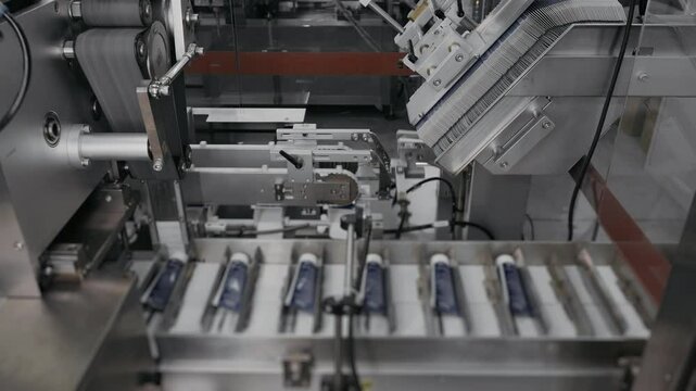 Automatic packaging of plastic tubes into cardboard boxes on factory conveyor