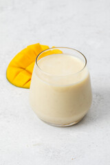 Refreshing mango smoothie in a glass with sliced mango on light background