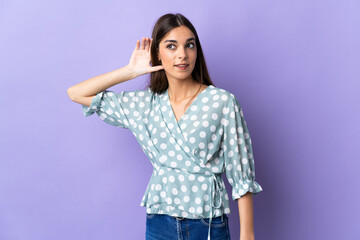 Young caucasian woman isolated on blue background listening to something by putting hand on the ear