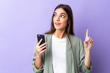 Fototapeta premium Young caucasian woman using mobile phone isolated on purple background intending to realizes the solution while lifting a finger up
