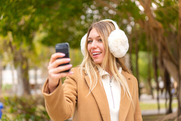 Young pretty blonde woman wearing winter muffs at outdoors making a selfie
