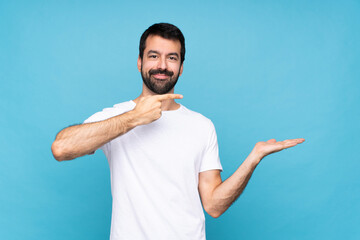 Young man with beard  over isolated blue background holding copyspace imaginary on the palm to insert an ad