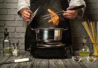 A chef uses a fork to lift chicken wings out of a pot as steam rises in a cozy kitchen. Various ingredients and kitchen utensils are neatly arranged around the stove