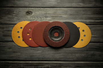 Different types of sanding discs are arranged on a rustic wooden surface, showcasing materials...