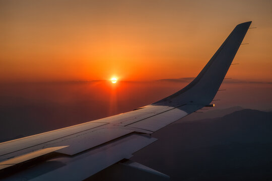 Beautiful view from airplane window on colorful orange sky with evening light and wing of plane
