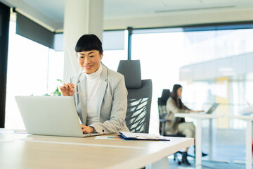 Fototapeta premium Professional Japanese woman working diligently at modern office space during bright daytime hours