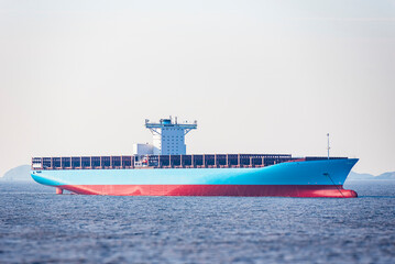 Newly painted, blue, large container ship without cargo on deck, anchored at open calm sea.