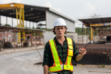 Civil male engineer is using walkie talkie and laptop to communicate with his coworkers or colleagues to manage a slab or precast floor production system in a factory.