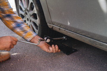 Changing flat tire using jack in parking lot during daylight with focus on hands and tools involved in process