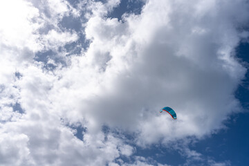 Colorful kite soaring high against blue sky with fluffy clouds during bright sunny day near the beach