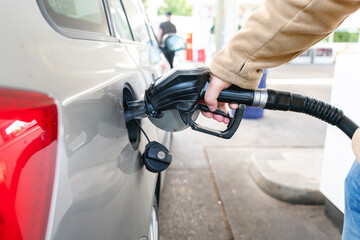 Filling gas at a fuel station in the afternoon under a clear sky with a busy atmosphere and multiple vehicles present nearby