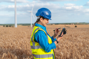 Female Engineer conducts field research in field near wind turbines making notes on tablet with a...