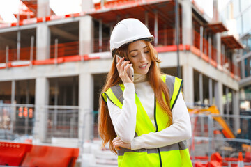 Young Female Construction site worker communicates on phone while wearing safety gear