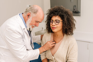Obraz premium Senior Caucasian doctor using stethoscope examining lungs and heart of young African american woman in medical clinic