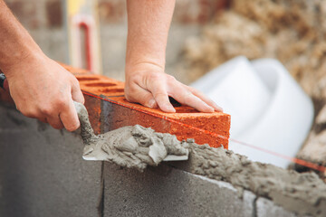 Close-up of hands of Bricklayer applying mortar to red brick while building wall at construction site 