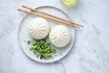 Freshly cooked chinese baozi and edamame beans, top view on a white stone background, horizontal shot