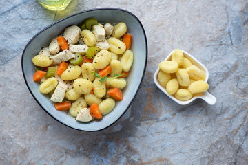 Bowl of chicken gnocchi soup on a blue and beige stone background, horizontal shot, view from above