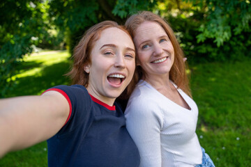Obraz premium Two friends mother and daughter enjoying sunny afternoon in green park while taking cheerful selfie together to capture their joyful moment