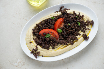 White plate with hummus and roasted ground beef on a light-beige stone background, horizontal shot, high angle view