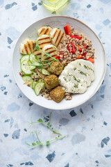 Plate with halloumi cheese, quinoa, falafel and vegetables, vertical shot on a white and blue granite background with space, above view