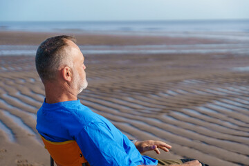 Relaxing moment by the calm sea on a sunny day, a man enjoying solitude and the sound of waves while seated on the beach at low tide