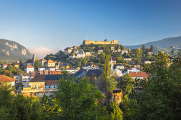 Fototapeta premium Jajce town in Bosnia and Herzegovina, Europe. Picturesque view of a European town nestled on a hillside with a historic fortress overlooking the houses, captured under a clear blue sky.