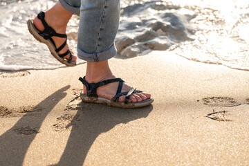 Footsteps in the sand at sunset on a beach in summer with water gently lapping at worn sandals