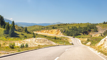 Road in Bosnia and Herzegovina, Europe. Scenic road winding through green hills beneath a clear blue sky, promising a journey filled with natural beauty and adventure.