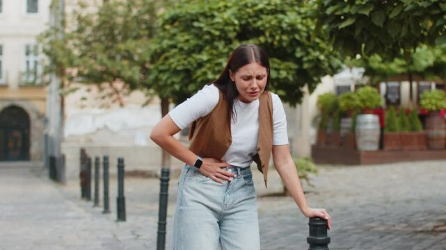 Caucasian young woman traveler feeling sudden strong abdominal stomach ache gastritis problem. Upset tourist lady having symptom poisoning diarrhea indigestion peptic ulcer pancreatitis on city street