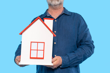 Man holds a miniature house model against  blue background while showcasing interest in home design...