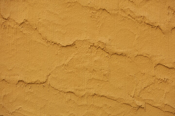 Rippled sand and beach caressing wave patterns appear in stucco surface of a sunglow orange colored wall. The warm earthy tones and uneven surface make the texture interesting and dynamic.