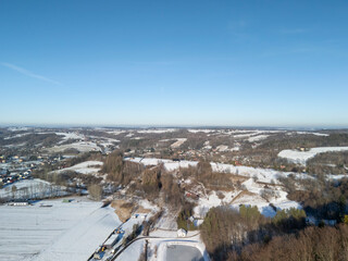 Aerial view of a winter landscape showcasing a serene countryside covered in snow, with scattered houses and trees under a clear blue sky.