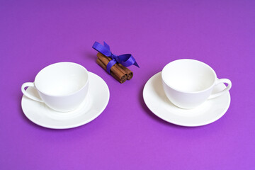 Two Empty White Cups with Cinnamon Sticks on a Purple Background