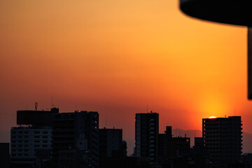 Silhouetted buildings adorn radiant orange sunset sky backdrop. A sliver of the glowing sun's orb...