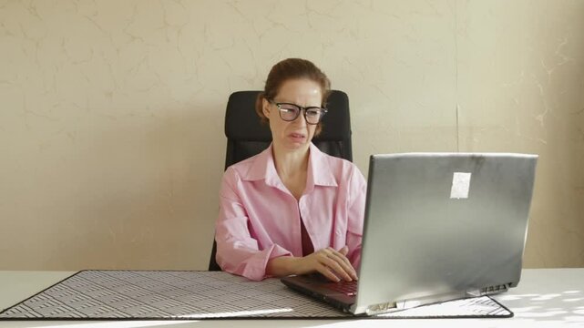 woman in office looking at laptop with disgust, adult female with glasses seated at a desk, aversion to digital remote work and technology