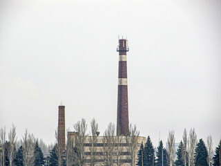 Image depicts an industrial scene, focusing on a tall, multi-colored chimney in a large complex or...