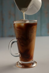 Pouring milk into glass with black coffee