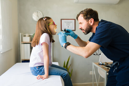 Pediatrician wearing blue medical gloves checking young patient's throat during pediatric medical examination in clinical setting