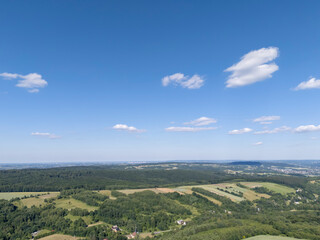 Fototapeta premium Aerial view of lush green fields under a clear blue sky, showcasing rolling hills and scattered clouds in a serene landscape. Ideal for nature-themed projects.
