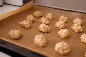 The raw dough, rolled into balls, is laid out on a baking sheet for making oatmeal cookies with...