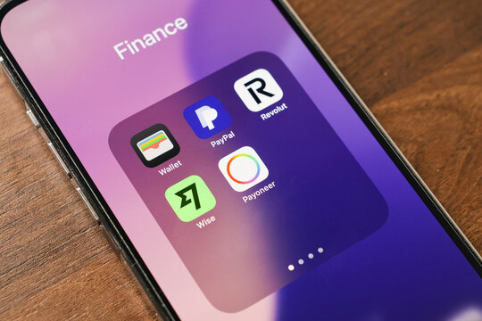 Poznan, Poland - March 12, 2025: smartphone screen showing finance apps folder with wallet, paypal, revolut, wise, and payoneer icons on wooden table background