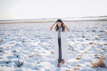 Happy young woman walking on snow covered meadow in winter sunny day.