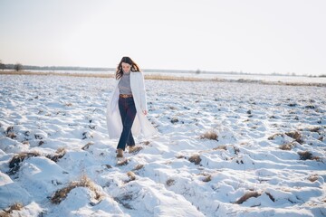 Happy young woman walking on snow covered meadow in winter sunny day.