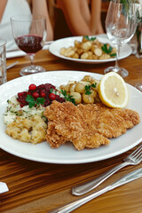 Elegant presentation of Austrian Wiener schnitzel with lemon, cranberry sauce, and potato salad at a European dining table