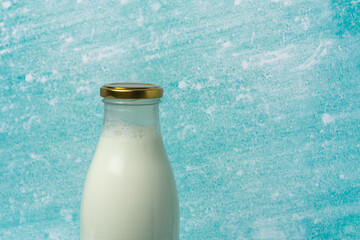Glass milk bottle with a golden cap, placed against a soft blue background. The image evokes...