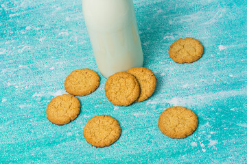 Glass bottle of milk sits next to scattered cookies. The cookies appear freshly baked, evoking a sense of comfort and indulgence. A warm, inviting scene perfect for food-related themes.