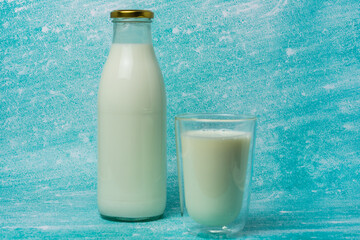 Full glass of milk sits next to a glass milk bottle on a blue surface. Scene evokes freshness and simplicity, perfect for dairy, breakfast, and healthy lifestyle themes.