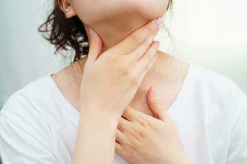 Asian woman touching her neck and throat for thyroid gland problem.