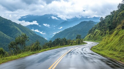 Fototapeta premium A damp, rain-soaked road through deep green mountains with low-hanging clouds