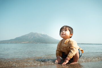 桜島をバックに浜辺で砂遊びをする一歳の男の子